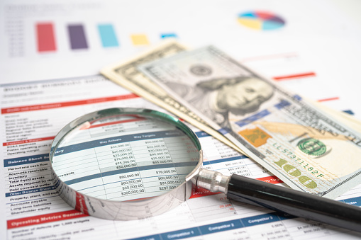 Magnifying glass and US dollar banknotes on spreadsheet and charts graphs paper. Financial development, Banking Account, Statistics, Investment Analytic research data economy.