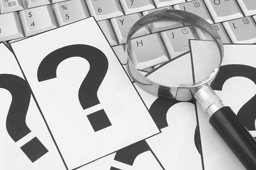 Magnifying glass with question marks on laptop computer keyboard. Questions and answers, internet search concept.