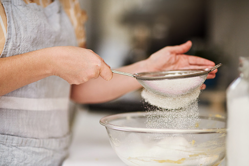Cropped shot of a woman sifting flour into a glass bowl