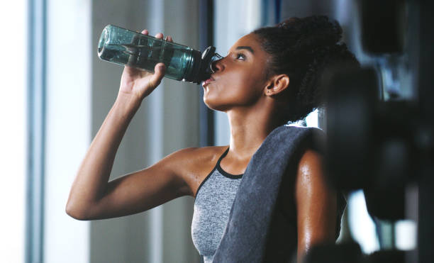 Make sure you stay hydrated throughout your session Shot of a sporty young woman drinking water while exercising at the gym drinking water in the gym stock pictures, royalty-free photos & images