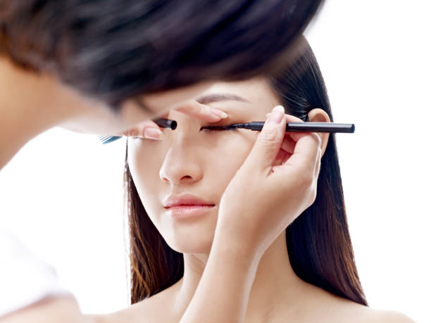 makeup artist working on a female asian model makeup artist working on eyeliner of a young asian model, isolated on white background. korean cosmetics stock pictures, royalty-free photos & images