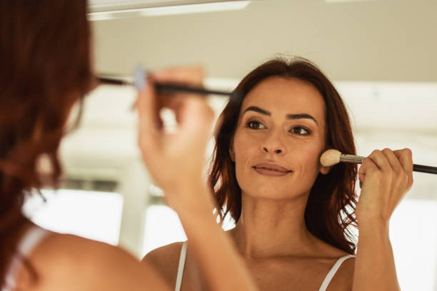 Make-up routine of a pretty woman Headshot of mature woman using a make-up brush to apply foundation on her cheeks. applying blush stock pictures, royalty-free photos & images