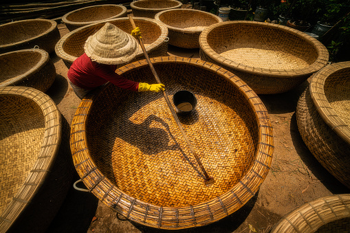 A woman worker is painting rotten oil on the basket boats, which make it