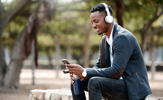 Shot of a young businessman using a smartphone and headphones in the city