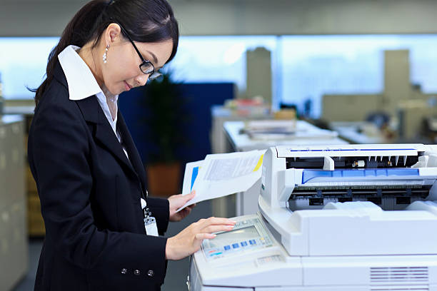 Making copies Real Japanese office - Japanese office lady at the photocopy machine xerox photocopy machine stock pictures, royalty-free photos & images