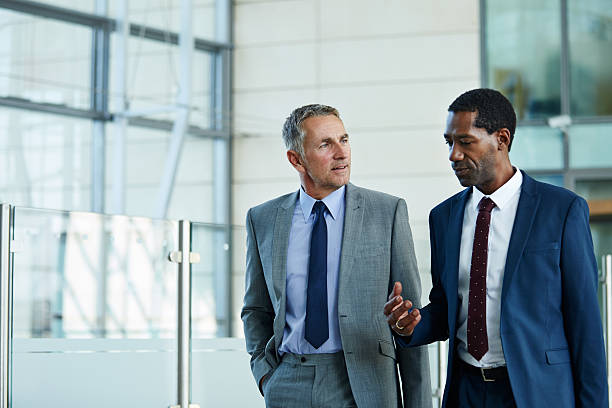 Making decision on the move Shot of two businessmen walking and talking together in the lobby of an office building business suit stock pictures, royalty-free photos & images