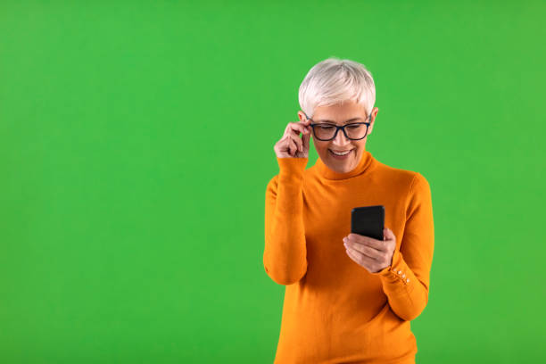 Making it easier for elders to tell their stories Photo an attractive mature woman using her phone against a green background smart phone green background stock pictures, royalty-free photos & images
