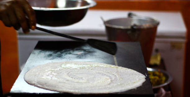Making of paper plain Dosa on a tawa pan by spreading dosa batter mix of rice and dal and oiling on the thin sheet Making of paper plain Dosa on a tawa pan by spreading dosa batter mix of rice and dal and oiling on the thin sheet thosai stock pictures, royalty-free photos & images