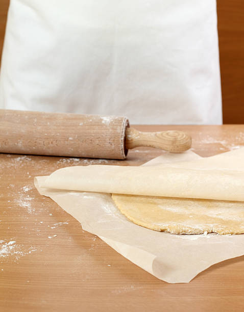 A baker rolling a dough between sheets of baking paper.