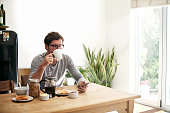 Shot of a young man having breakfast and using a phone at home