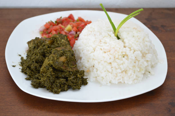 Malagasy dish from Madagascar : pounded cassava leaves and pork meat with rice and tomatoes salad dressing stock photo