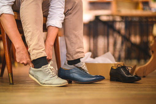 Close-up shot of a male adult shopping and trying on casual light color shoes in a menswear clothing store. He ordered three different models to try on but he will buy the most comfortable pair of shoes for everyday use.