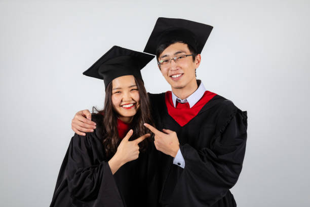 Male and female graduate students pointing each other in gowns and mortarboards Male and female graduate students stand together pointing at each other happy to finish studies in gowns and mortarboards posing on white background bachelor degrees stock pictures, royalty-free photos & images
