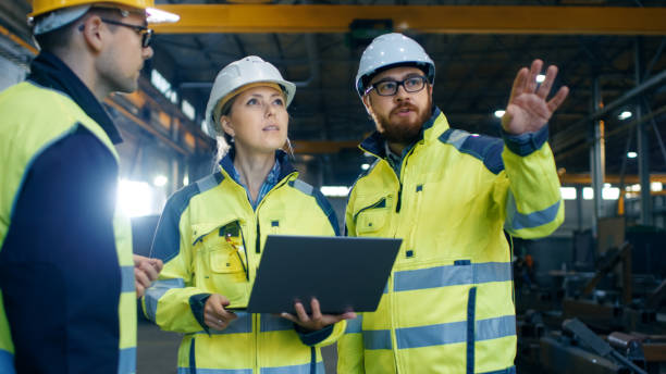 Male and Female Industrial Engineers Talk with Factory Worker while Using Laptop. They Work at the Heavy Industry Manufacturing Facility. Male and Female Industrial Engineers Talk with Factory Worker while Using Laptop. They Work at the Heavy Industry Manufacturing Facility. metalwork stock pictures, royalty-free photos & images