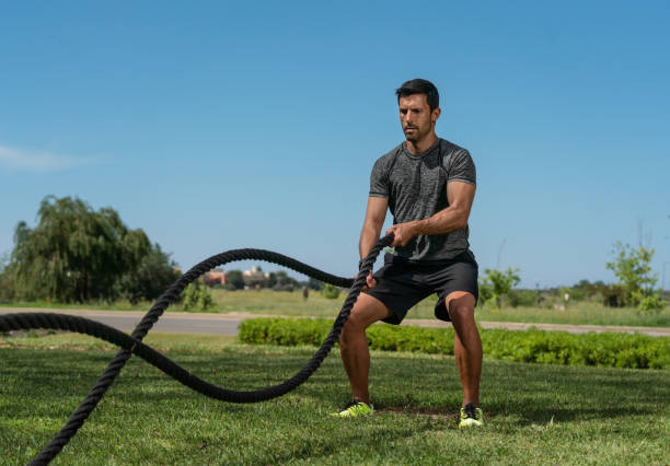 Male athlete on the outdoor in the park, exercises for endurance, using a thick rope, for cross fitness. European Caucasian stock photo