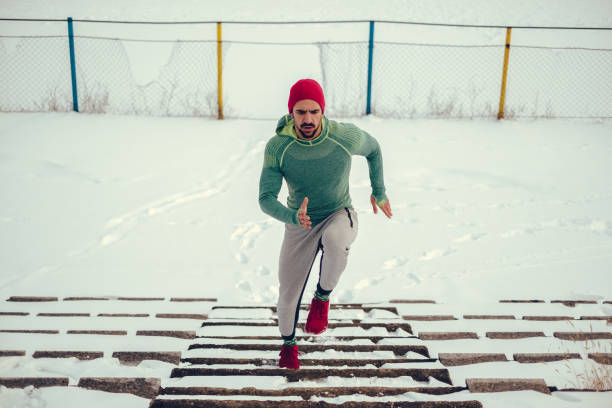 Male athlete with red hat running up the snowy stairs stock photo