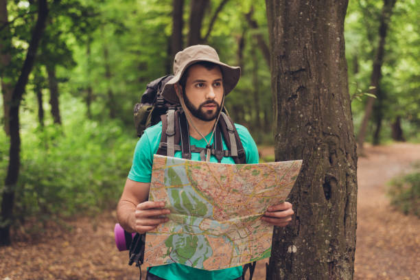 Male brunet bearded confused tourist got lost in the forest, holding map, looking far, trying to find the way. He has a backpack, all needed for overnight stay. Search the trail way Male brunet bearded confused tourist got lost in the forest, holding map, looking far, trying to find the way. He has a backpack, all needed for overnight stay. Search the trail way boy scout camp stock pictures, royalty-free photos & images