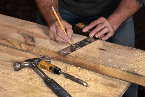 Male carpenter marks a line on a wooden board to cut while on construction job site stock photo