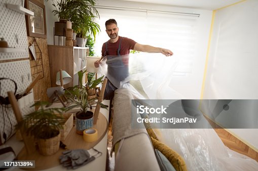 istock Male construction worker, covering the furniture with protective plastic foil 1371313894