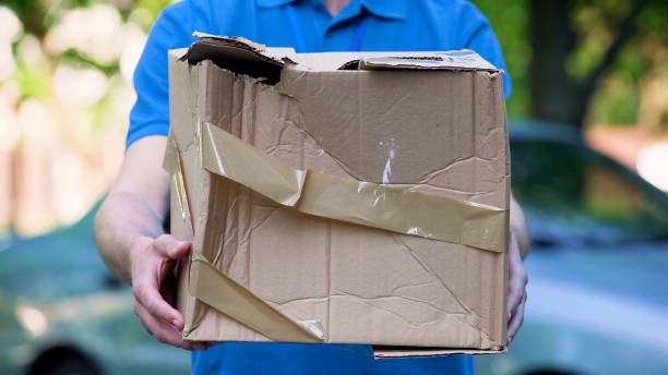 Male courier showing damaged box, cheap parcel delivery, poor shipment quality stock photo