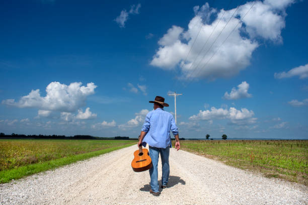 Male cowboy walking down country road with guitar stock photo