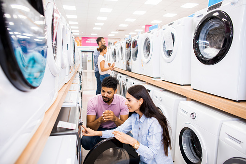 Young female salesperson assists to a male customer with a washing machine in a home appliances store.