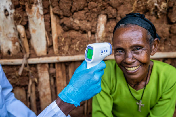 Male doctor taking senior woman temperature in remote village, East Africa stock photo