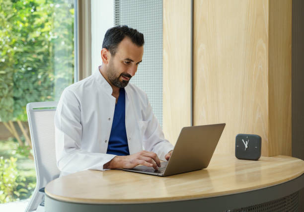 Male doctor working on laptop in his clinic stock photo