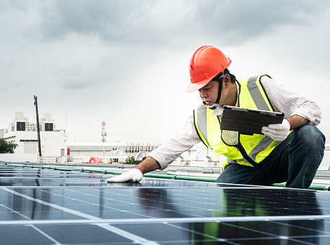 male engineer checks a photovoltaic (solar) plant and uses a recording tablet. mechanic in protective helmet. Man in uniform holding tablet.