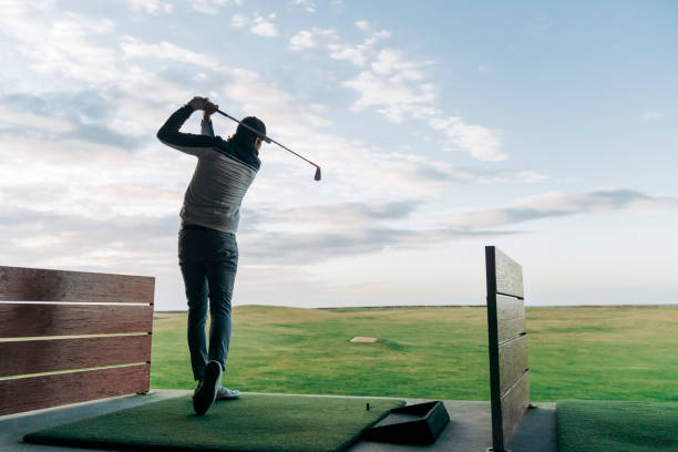 Male golfer swinging club at course against sky stock photo
