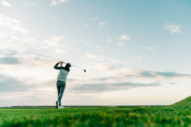 Male golfer swinging club at course during sunset stock photo