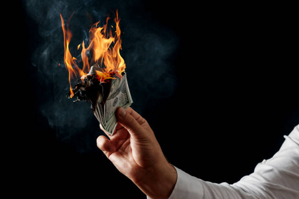 Male hand close-up, holds burning money in hands, burning US dollars. Black background, isolate. The concept of inflation, a decrease in the purchase of foreign currency, and devolution. stock photo