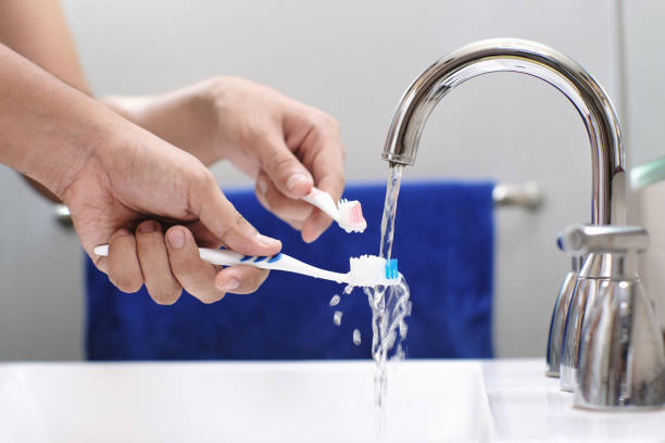 Male Hand Rinsing Toothbrush With Water In Bathroom stock photo