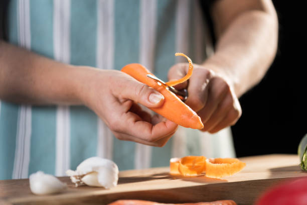 Male hands peeling fresh orange carrot. Root vegetable processing in kitchen. stock photo