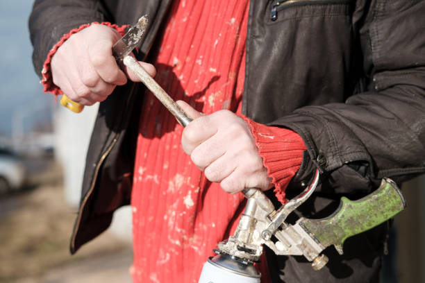Male hands repair an old, defective professional gun, for aerosol insulating foam, with a knife. stock photo