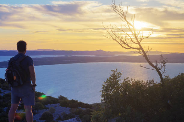 Male hiker on top of the hill watching a beautiful sunset over Adriatic sea stock photo