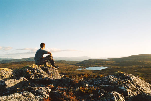 Male hiker sitting on rocks looking out over a marshland viewpoint in nature stock photo