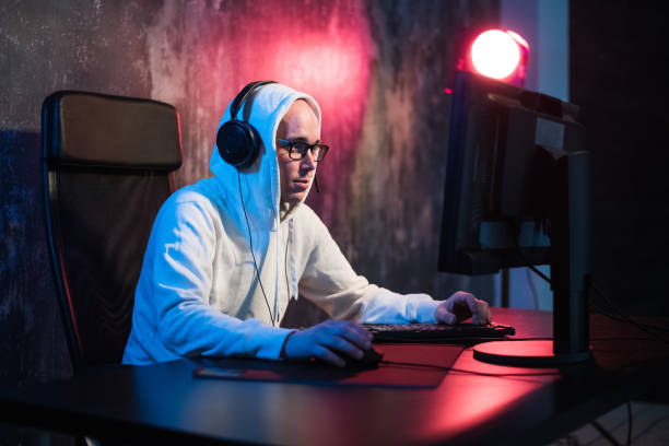 male hooded gamer playing online game on pc computer male hooded gamer playing online game on computer. gaming computer desk stock pictures, royalty-free photos & images