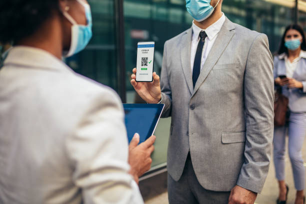 Male office worker in safety mask showing electronic vaccination certificate to employer stock photo