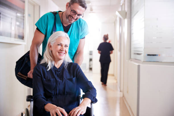 Male Orderly Pushing Senior Female Patient Being Discharged From Hospital In Wheelchair Male Orderly Pushing Senior Female Patient Being Discharged From Hospital In Wheelchair leaving stock pictures, royalty-free photos & images