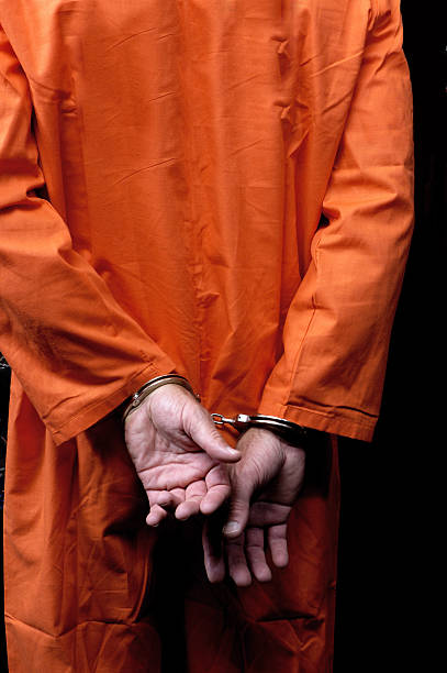 Male prisoner in orange suit his arms handcuffed behind back stock photo