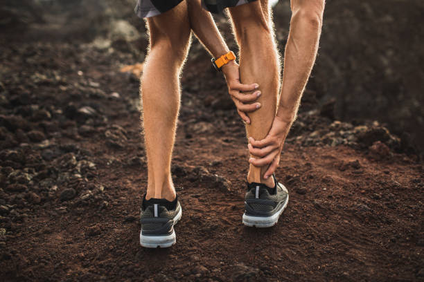 Male runner holding injured calf muscle and suffering with pain. Sprain ligament while running outdoors. View from the back close-up. stock photo