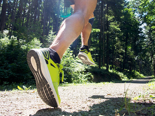 Male runner running on road through forest. Focus on leg. stock photo