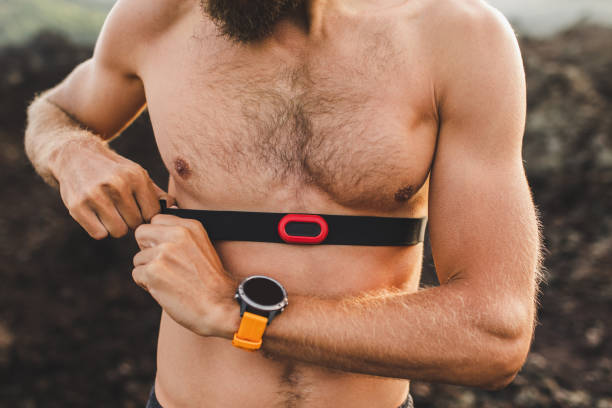 Male runner wearing professional chest heart rate monitor and preparing for trail running outdoors. Topless body close-up and smart watch or fitness tracker on hand. stock photo