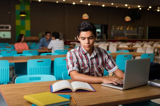 Male student typing on computer from book stock photo
