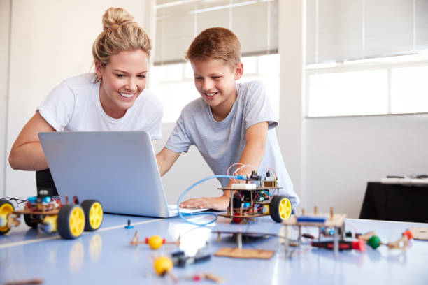 Male Student With Teacher Building Robot Vehicle In After School Computer Coding Class Male Student With Teacher Building Robot Vehicle In After School Computer Coding Class programming languages to teach kids stock pictures, royalty-free photos & images