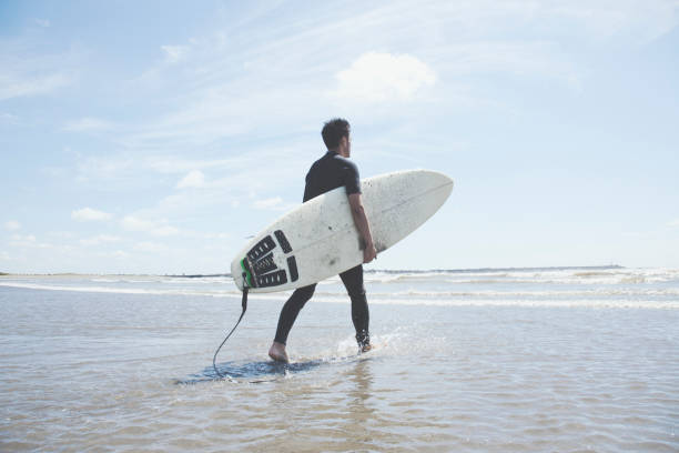 ビーチを歩いてサーフィン ボードを持って男性のサーファー - サーフィン ストックフォトと画像