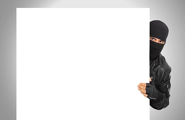 Male thief wearing black hiding behind white panel stock photo