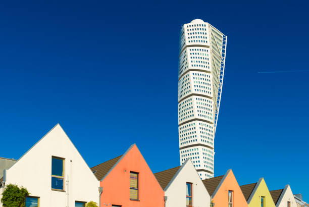 Malmo, Sweden: View of The Turning Torso skyscraper with blue sky on the background and a row of colored residential houses in front stock photo