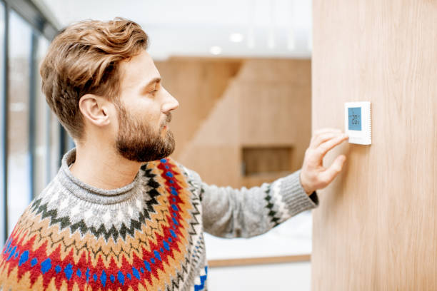 Man adjusting temperature with thermostat at home Man in sweater feeling cold adjusting room temperature with electronic thermostat at home thermostat stock pictures, royalty-free photos & images
